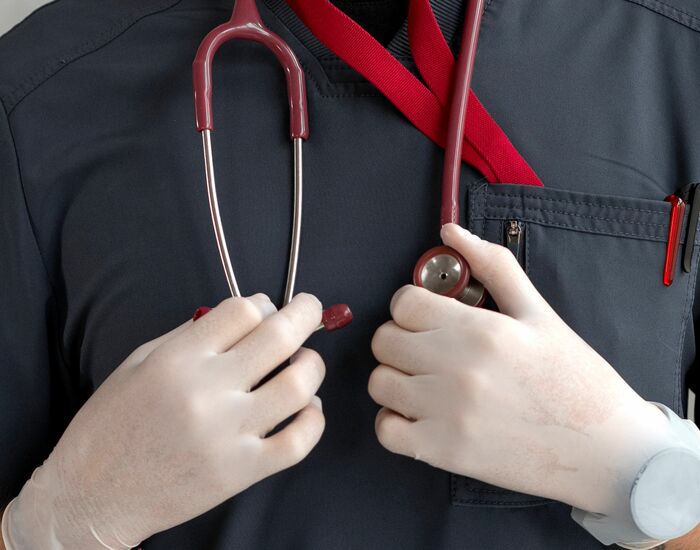 Oberkörper-Aufnahme einer Person in Pflegemontur mit Stethoskop und medizinischen Handschuhen